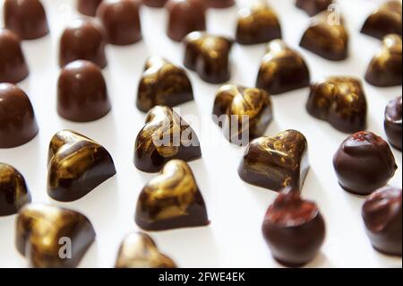 Auswahl an schönen belgischen Pralinen, Trüffeln und Pralinen mit goldenem Ornament in Herzform auf weißem HintergrundA Stockfoto