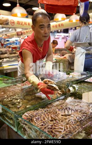 Ein Fischhändler präsentiert einem Kunden Proben seiner Krabben an seinem Stand im Tai Yuen Market in Hongkong. Stockfoto