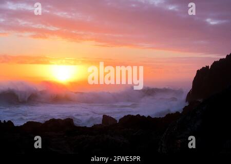 Goldener Sonnenuntergang entlang der felsigen Küste von Tsitsikamma in Südafrika, mit einem rauhen stürmischen Meer im Vordergrund. Stockfoto