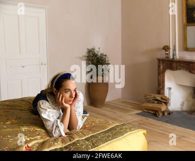 Dutch Master Stil Porträt einer schönen jungen Frau in authentische Renaissance Kostüm liegen auf einem luxuriösen antiken Himmelbett in einem goldenen Schlafzimmer eines Stockfoto