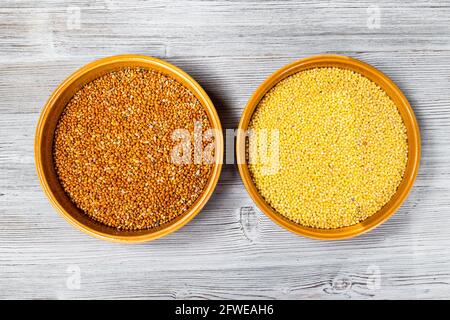 Draufsicht auf ganze und polierte Proso Hirse Körner in Runde Keramikschalen auf grauem Holztisch Stockfoto