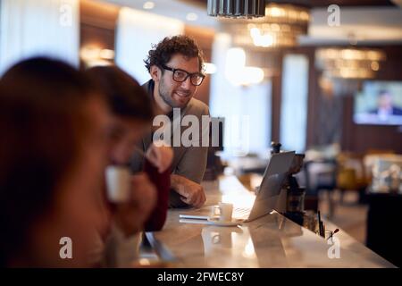 Junger, gutaussehender kaukasischer Geschäftsmann, der an einer Bar arbeitet und Kaffee trinkt Stockfoto