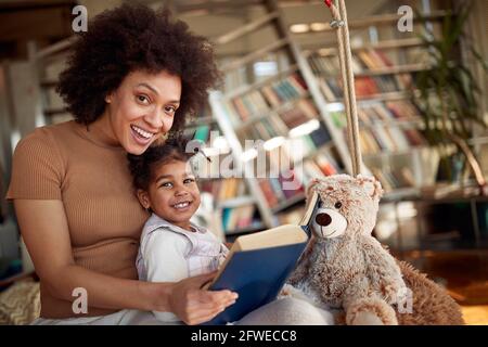 Eine junge, schöne Mutter und ihre kleine Tochter sind voller Freude, während sie in entspannter Atmosphäre zu Hause gemeinsam auf der Schaukel posieren. Familie, gemeinsam, Stockfoto