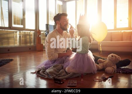 Der junge Vater ist voller Freude, als seine Tochter ihn schminke, während sie sich zu Hause in entspannter Atmosphäre auf ein Balletttraining vorbereite. F Stockfoto