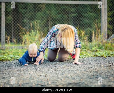 Mama spielt mit dem Kind, das auf dem Bürgersteig sitzt. Familie auf einem Spaziergang. Stockfoto