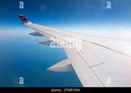 Flugzeugflügel mit Schweizer Logo-Flagge / Flugzeugflügel einer Bombardier C-Serie und Blick auf das Meer und die Küste aus seiner Reisehöhe über die Küste Frankreichs an einem klaren Tag mit blauem Himmel. (100) Stockfoto