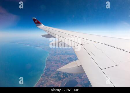 Flugzeugflügel mit Schweizer Logo-Flagge / Flugzeugflügel einer Bombardier C-Serie und Blick auf das Meer und die Küste aus seiner Reisehöhe über die Küste Frankreichs an einem klaren Tag mit blauem Himmel. (100) Stockfoto