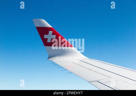 Flugzeugflügel mit Schweizer Logo-Flagge / Flugzeugflügel einer Bombardier C-Serie und Blick auf den sonnigen blauen Himmel auf Reisehöhe an einem klaren Tag mit blauem Himmel. (100) Stockfoto