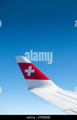 Flugzeugflügel mit Schweizer Logo-Flagge / Flugzeugflügel einer Bombardier C-Serie und Blick auf den sonnigen blauen Himmel auf Reisehöhe an einem klaren Tag mit blauem Himmel. (100) Stockfoto