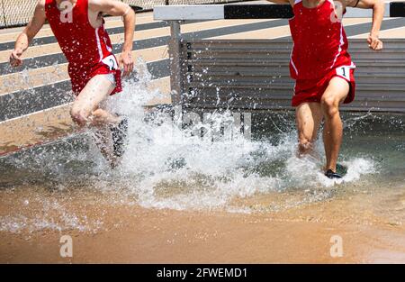 Zwei Läufer, die in einer High School-Hindernislauf plantschen in der Wassergrube, während sie versuchen, das Wasser zu verlassen. Stockfoto