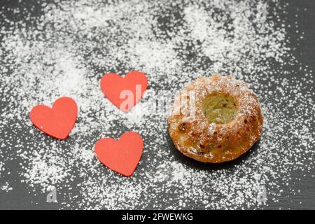 Runder Kuchen mit rotem Herz und Puderzucker auf Schwarz Platte Stockfoto