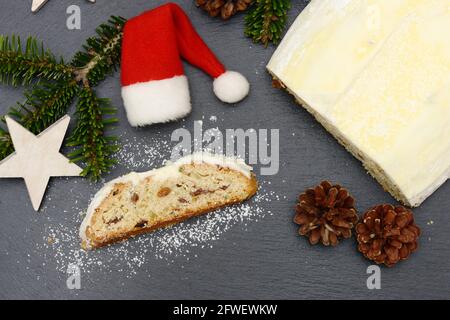 weihnachtsstollen mit Tannenzweig, Tannenzapfen, Sternen und weihnachtsmütze, der zur weihnachtszeit auf schwarzem Schiefer liegt Stockfoto