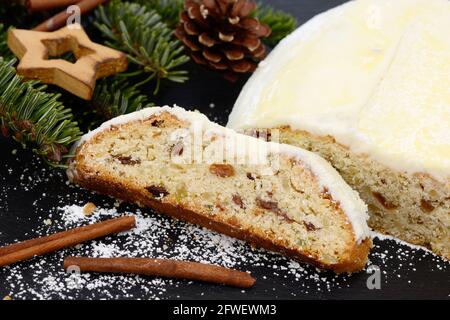 weihnachtsstollen mit Tannenzweig, Tannenzapfen, Sternen und Zimtstangen, die zur weihnachtszeit auf schwarzem Schiefer liegen Stockfoto