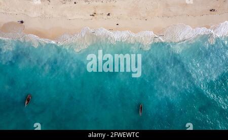 Luftaufnahme des weißen Sandstrandes und des smaragdgrünen Wassers mit Fischerbooten, die auf den Wellen des indischen Ozeans auf der Insel Sansibar, Tansania, schwimmen. Stockfoto