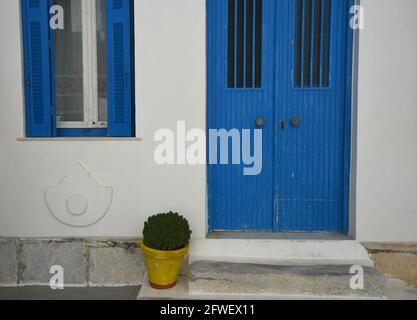 Ländliche Haus malerische Fassade mit einer blauen Holztür und Fensterläden auf einer weißgetünchten Wand in Amorgos Insel, Kykladen Griechenland. Stockfoto