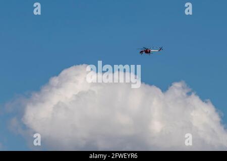 Ein großer rot-weißer Feuerwehrhubschrauber fliegt hinein Der Himmel über einer Wolke für eine Feuerrettung Stockfoto