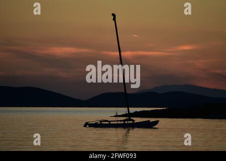 Sonnenuntergangs-Landschaft mit Panoramablick auf eine Silhouette eines Segelbootes auf den Gewässern der Insel Amorgos in den Kykladen, Griechenland. Stockfoto