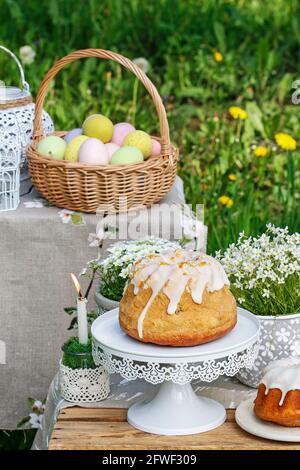 Traditioneller Osterkuchen und Korb mit bunten Eiern im Garten. Festliche Einrichtung Stockfoto