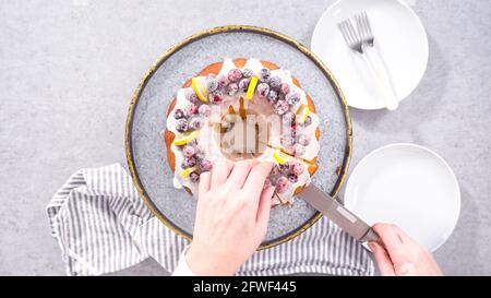 Flach liegend. Schritt für Schritt. Schneiden von Zitrone Cranberry Bundt Kuchen mit Zucker Cranberries und Zitronenkeile verziert. Stockfoto