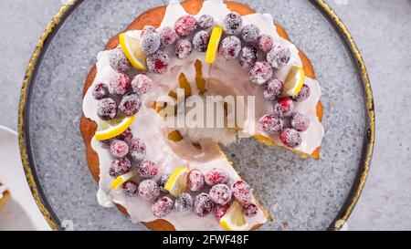 Flach liegend. Schritt für Schritt. Schneiden von Zitrone Cranberry Bundt Kuchen mit Zucker Cranberries und Zitronenkeile verziert. Stockfoto