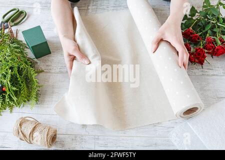 Floristin bei der Arbeit: Frau zeigt, wie man ein Blumenarrangement mit roten Rosen und Thuja-Zweigen, Schritt für Schritt, Tutorial. Stockfoto