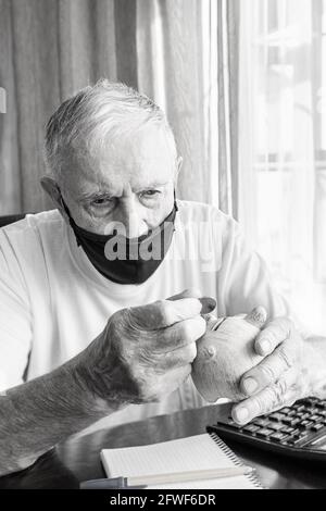 Der alte Mann in einer medizinischen Maske zählt Pennys aus der Pensionskasse. Ein besorgter älterer Mann steckt Geld in eine Sparschwein. Auswirkungen der Sperrung auf die Wirtschaft und Stockfoto