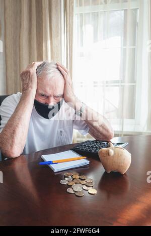 Der alte Mann in einer medizinischen Maske zählt Pennys aus der Pensionskasse. Ein besorgter älterer Mann steckt Geld in eine Sparschwein. Auswirkungen der Sperrung auf die Wirtschaft und Stockfoto