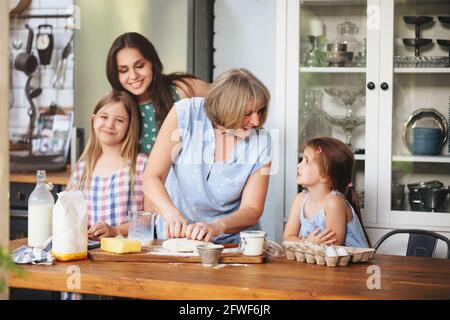 Glückliche Erwachsene und reife Frauen kochen zusammen mit netten Mädchen Am Tisch in der Küche Stockfoto