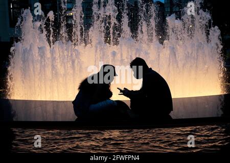 Ein Paar sitzt am Brunnen am Josie Robertson Plaza in New York, USA. Mai 2021. Das Lincoln Center der Stadt, in dem ein 14,000 Quadratmeter großer Teppich aus Kunstrasen eingerichtet wurde. Der Rasen, der vom renommierten Bühnenbildner Mimi Lien entworfen wurde, besteht aus recycelbarem, biobasierten SYNLawn und wird im Rahmen des Programms „Restart Stages“ für Aufführungen im Lincoln Center verwendet, das die Verbindung zur Kunst wieder anregen soll, wenn die Stadt aus der Pandemie herauskommt. Quelle: Adam Stoltman/Alamy Live News Stockfoto