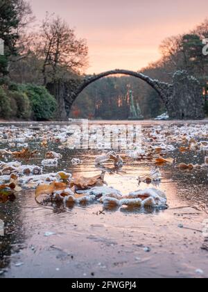 Frostige Nacht mit Vollmondlicht. Gefrorener See mit bunten Blättern, rund um die Rakotzbrücke, die Teufelsbrücke, im hellen Morgennebel. Kromlau Park, G Stockfoto