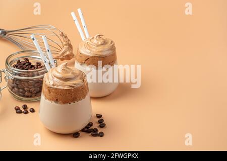 Ein belebendes, erfrischendes Kaffeegetränk in zwei Gläsern auf orangefarbenem Hintergrund. Seitenansicht, Kopierbereich. Dalgona Kaffee. Stockfoto