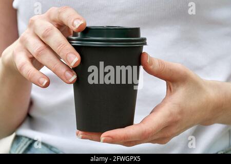 Schwarze Papptasse in Nahaufnahme mit Kaffee in den Händen der Frau. Modell Stockfoto