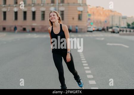 Lächelnde dunkelhaarige junge Frau genießt Rollerblading, wie Hobby aussieht In die Ferne trägt Sportlothes fährt schnell auf Rollen Stockfoto