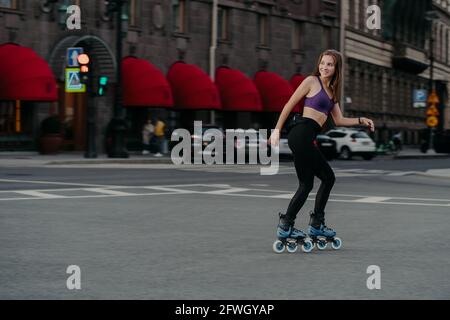 Schlanke Frau mit 3/4-Oberteil und Leggings mit Rollerblades durch Stadt genießt eine ausgezeichnete körperliche Training verbrennt Kalorien bekommt Energie entlastet Stress Stockfoto