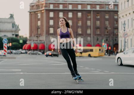 Sportlich schlanke Frau in aktiver Kleidung Fahrten auf Klingen genießt Outdoor-Fitness-Aktivität während warmen Sommertag Posen auf städtischen Platz auf Asphalt. Rollerblading Stockfoto