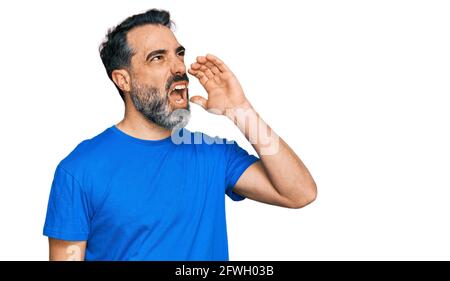 Mann mittleren Alters mit Bart trägt lässiges blaues T-Shirt und schreit laut zur Seite mit der Hand auf dem Mund. Kommunikationskonzept. Stockfoto