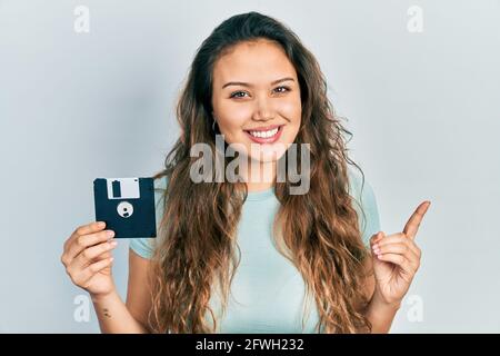 Junge hispanische Mädchen hält Diskette lächelnd glücklich zeigt mit Hand und Finger zur Seite Stockfoto