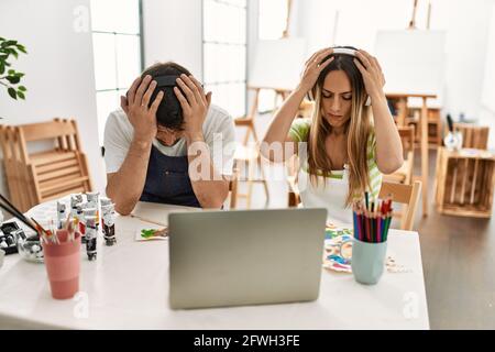 Junges Ehepaar und Ehemann im Kunststudio, das Video auf dem Laptop ansieht und an Kopfschmerzen leidet, verzweifelt und gestresst, weil Schmerzen und Migräne. Ha Stockfoto