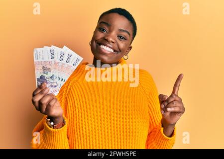 Junge afroamerikanische Frau mit isländischen Kronen-Banknoten lächelnd Zeigt mit Hand und Finger zur Seite Stockfoto