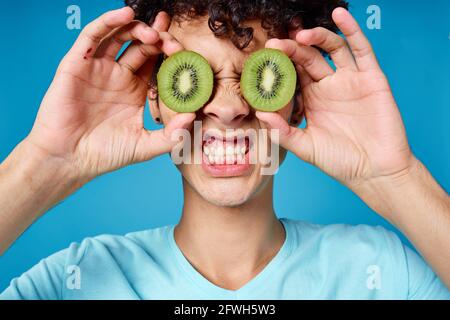 Mann mit lockigem Haar, der Kiwi in der Nähe des Klassengesichts hält Stockfoto