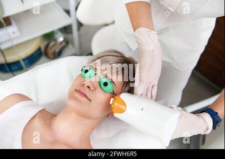 Nahaufnahme einer Kosmetikerin, die in einem Schönheitssalon Laser-Verjüngung macht. ELOS Epilation Haarentfernung Verfahren auf junge Frau Gesicht. Gesichtspflege. Hardwar Stockfoto