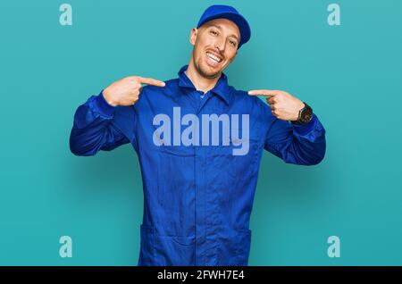 Glatze Mann mit Bart tragen Baumeister Jumpsuit Uniform sieht zuversichtlich mit Lächeln auf dem Gesicht, zeigt sich mit den Fingern stolz und glücklich. Stockfoto