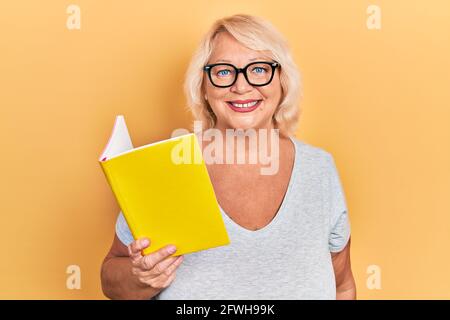 Blonde Frau mittleren Alters, die ein Buch liest, das positiv und Glücklich stehen und lächeln mit einem selbstbewussten Lächeln, das Zähne zeigt Stockfoto