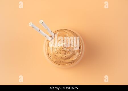 Ein Glas mit Kaffee-Dessert und Trinkhalmen auf orangefarbenem Hintergrund. Draufsicht, Nahaufnahme. Dalgona Kaffee. Stockfoto