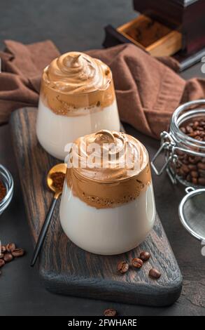 Erfrischender Dalgona Kaffee in zwei klaren Gläsern auf braunem Hintergrund. Seitenansicht, vertikal. Stockfoto