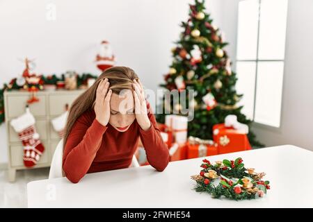 Kaukasische junge blonde Frau sitzt auf dem Tisch von weihnachtsbaum leiden unter Kopfschmerzen verzweifelt und gestresst, weil Schmerzen und Migräne. Hände auf Stockfoto