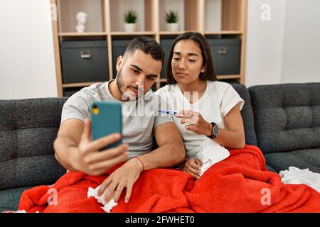 Junges lateinamerikanisches krankes Paar, das zu Hause eine medizinische Fernsultation mit dem Smartphone hat. Stockfoto