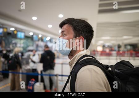 Maskierter Mann nutzt das Telefon und hält die Entfernung im Check-in-Bereich für den Flug am Flughafen in Zypern, Paphos City, beim Check-in. Reisen mit dem Flugzeug während der Fahrt Stockfoto