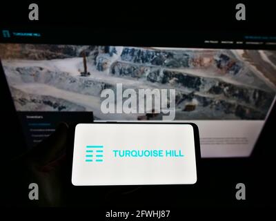 Person, die Mobiltelefon mit dem Logo des kanadischen Bergbauunternehmens Turquoise Hill Resources Ltd auf dem Bildschirm vor der Webseite hält. Konzentrieren Sie sich auf die Telefonanzeige. Stockfoto