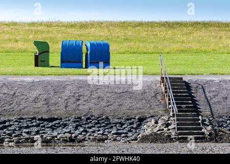 Steintreppen führen vom Strand zum grünen Deich auf Pellworm. Es gibt drei Liegen in blau und grün Stockfoto